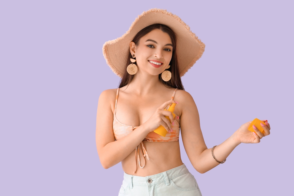 young,woman,applying,sunscreen,cream,on,lilac,background
